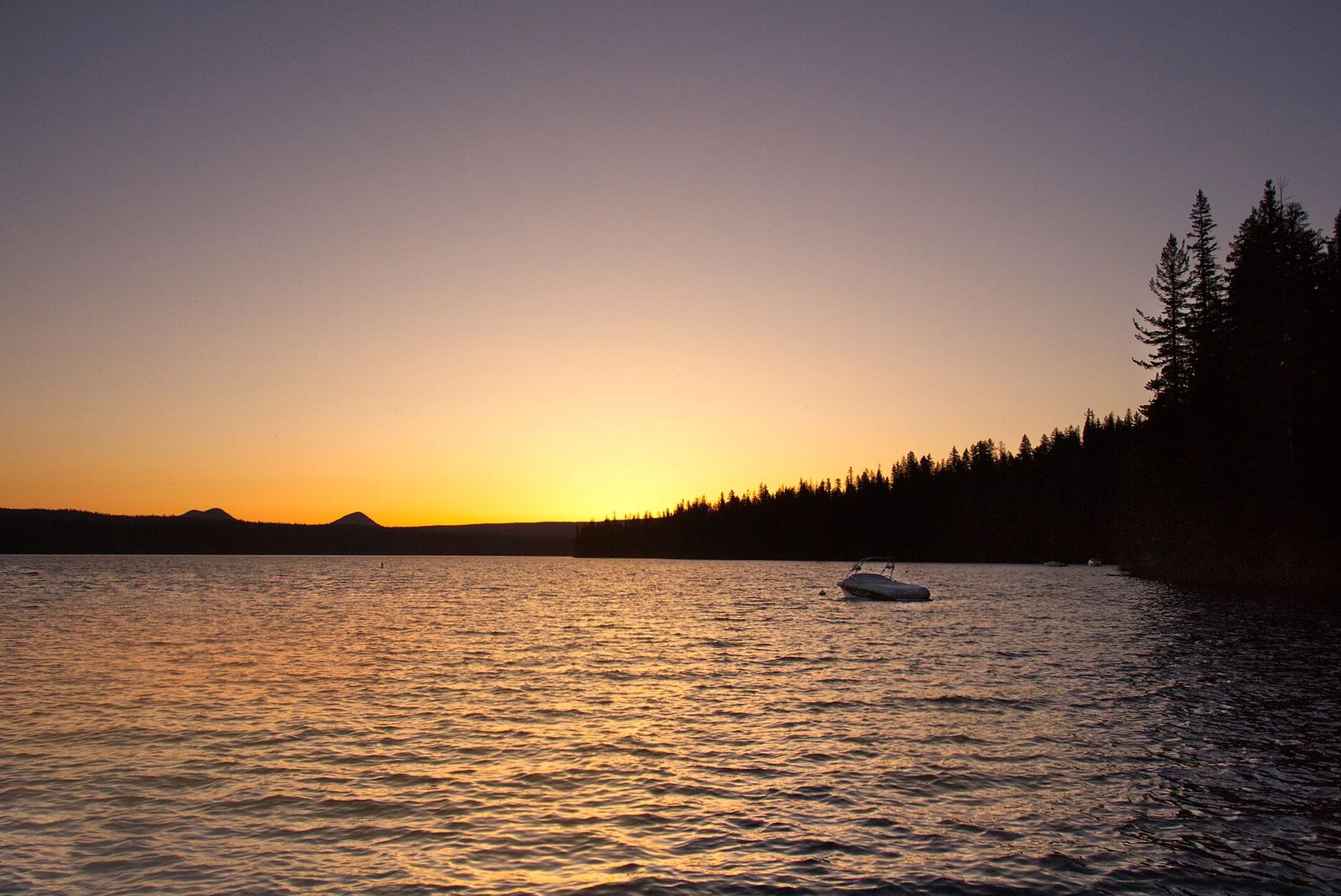 A calm lake at sunset bordered by forested hills